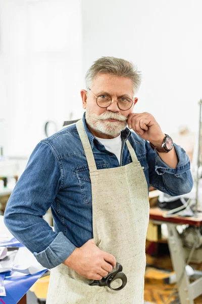 Middle aged male craftsman in apron looking at camera and posing at workshop — Stock Photo