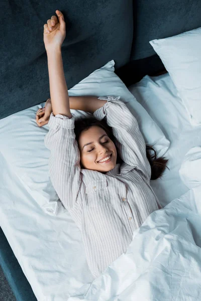 Happy girl in pajamas waking up and stretching in bed in the morning — Stock Photo