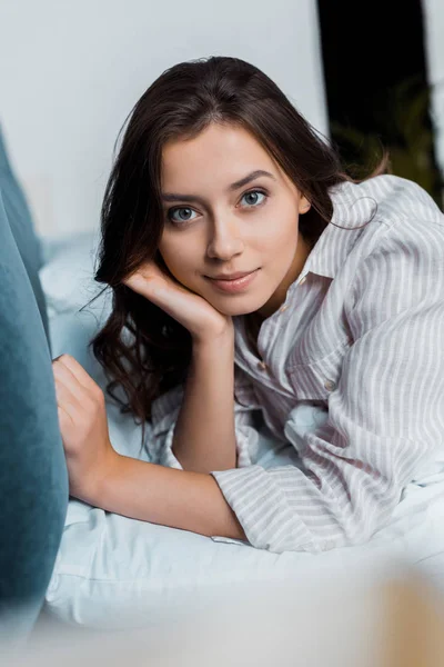 Hermosa joven en pijama mirando a la cámara y acostada en la cama - foto de stock
