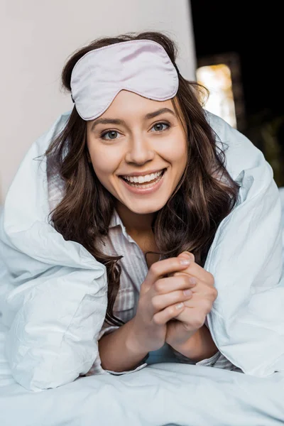 Beautiful happy girl in sleeping mask lying in bed — Stock Photo