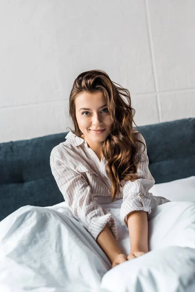 Attraktive lächelnde junge Frau, die morgens auf dem Bett sitzt — Stockfoto