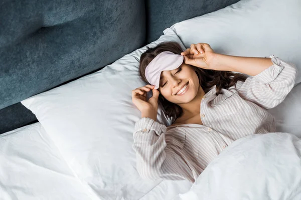 Menina feliz atraente em dormir máscara ocular relaxante na cama pela manhã — Fotografia de Stock