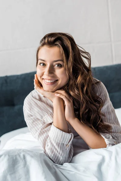 Cheerful young woman looking at camera and sitting on bed in the morning — Stock Photo