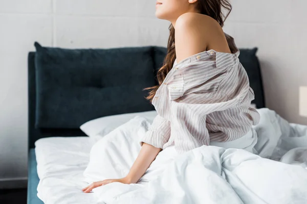 Vista recortada de la tierna mujer en pijama sentada en la cama por la mañana - foto de stock