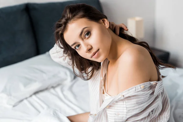 Schöne zarte Frau, die in die Kamera schaut und morgens auf dem Bett sitzt — Stockfoto