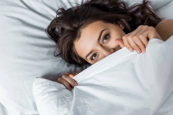 Schöne glückliche Frau versteckt sich unter einer weißen Decke auf dem Bett — Stockfoto