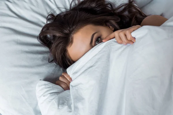 Attraktives Mädchen versteckt sich unter weißer Decke auf dem Bett — Stockfoto