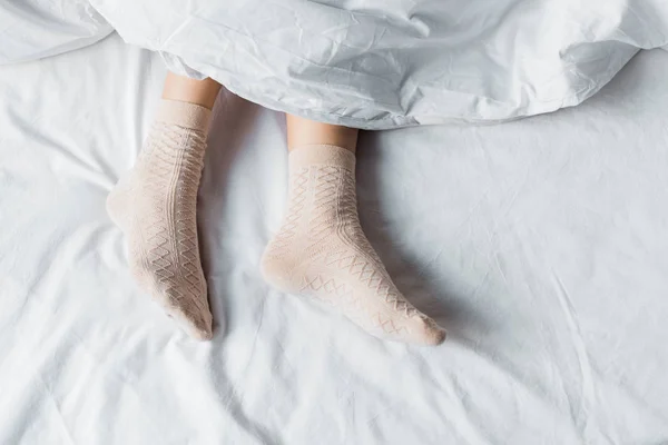 Top partial view of girl in socks lying under white blanket in bed — Stock Photo