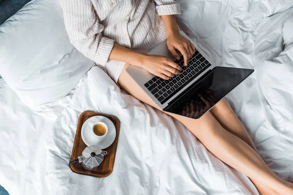 Vista cortada da mulher com xícara de café e panela moka usando laptop na cama pela manhã — Fotografia de Stock