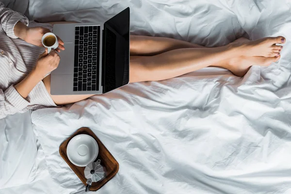 Vue de la section basse de la femme avec café du matin en utilisant un ordinateur portable au lit — Photo de stock