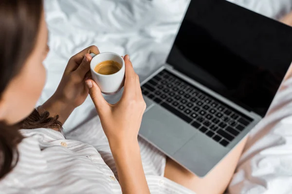 Vista recortada de la mujer con taza de café usando el ordenador portátil con la pantalla en blanco en la cama - foto de stock