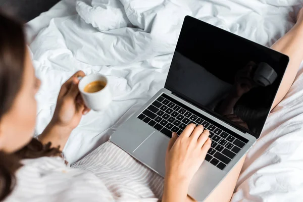 Vista parcial de la mujer sosteniendo la taza de café y el uso de ordenador portátil con pantalla en blanco - foto de stock