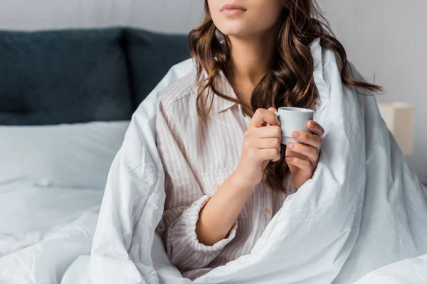 Vista recortada de chica con taza de café en la cama por la mañana - foto de stock