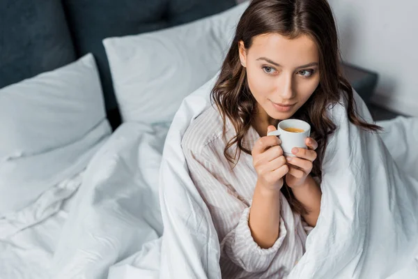 Beautiful pensive girl having coffee in bed in the morning — Stock Photo