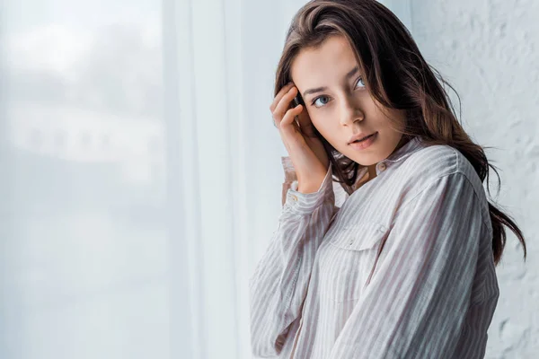 Young tender woman in pajamas standing near window and looking at camera — Stock Photo
