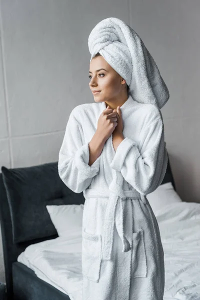 Belle femme rêveuse en peignoir blanc et serviette debout dans la chambre — Photo de stock