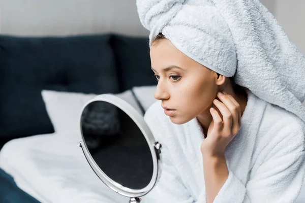 Belle femme en peignoir blanc et serviette en regardant sa peau dans le miroir — Photo de stock