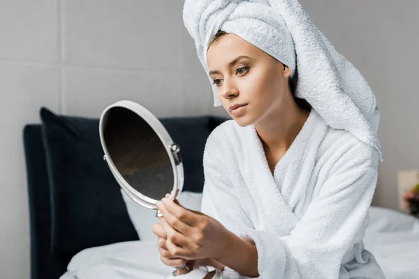 Beautiful woman in white bathrobe and towel looking in mirror — Stock Photo