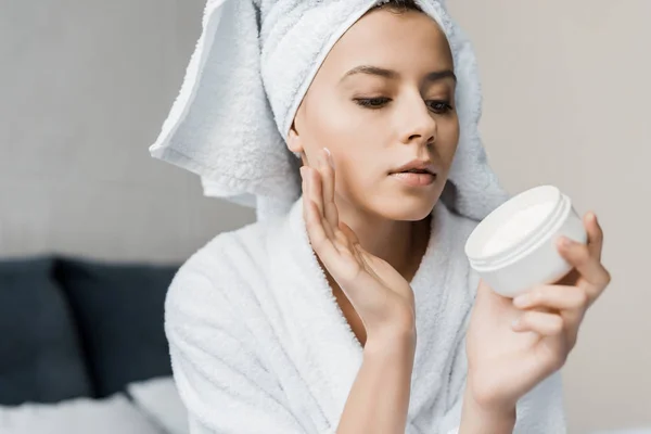 Bela jovem mulher aplicando creme cosmético no rosto — Fotografia de Stock