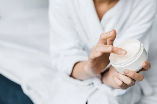 Partial view of girl with cosmetic cream in plastic container — Stock Photo