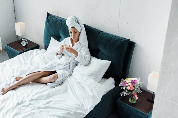 Beautiful girl in bathrobe and white towel holding cup of coffee in bedroom in the morning — Stock Photo