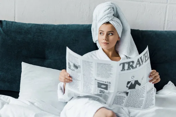 Hermosa chica con toalla en la cabeza leyendo periódico de viaje en la cama - foto de stock