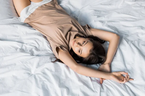 Belle jeune femme en pyjama reposant sur le lit le matin — Photo de stock