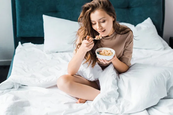 Attraktives Mädchen isst Haferflocken zum Frühstück im Bett — Stockfoto