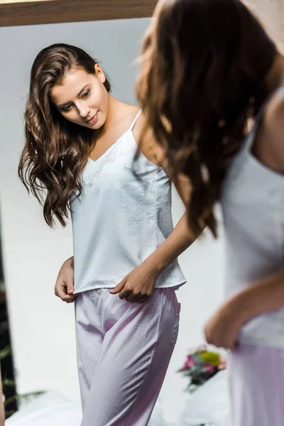 Schönes schlankes Mädchen im Pyjama, das ihr Spiegelbild im Spiegel betrachtet — Stockfoto