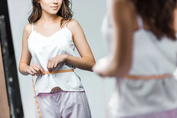 Cropped view of woman measuring her waistline and looking at mirror — Stock Photo