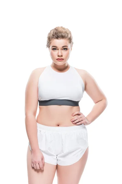 Young oversize woman in sportswear standing with hand on waist and looking at camera isolated on white — Stock Photo