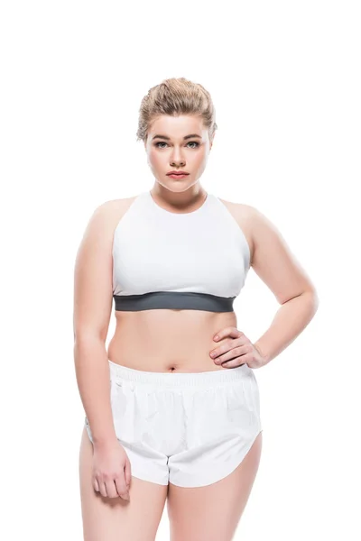 Jeune femme oversize en vêtements de sport debout avec la main à la taille et en regardant la caméra isolée sur blanc — Photo de stock