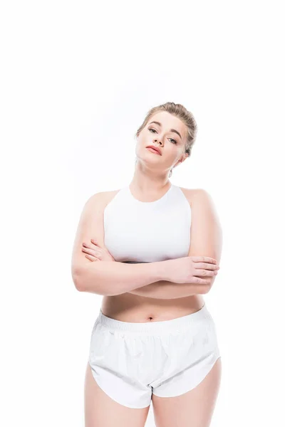 Jeune femme en surpoids en tenue de sport debout avec les bras croisés et regardant la caméra isolée sur blanc — Photo de stock