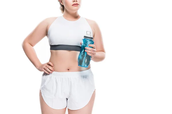 Обрезанный снимок крупногабаритной девушки в спортивной одежде с бутылкой воды, изолированной на белом — стоковое фото