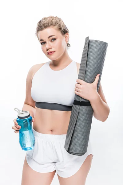 Красива дівчина з надмірною вагою тримає пляшку води та йога килимок ізольовано на білому — стокове фото