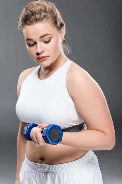 Jeune taille plus femme faisant de l'exercice avec haltère isolé sur gris — Photo de stock