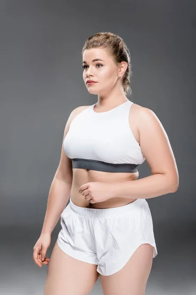 Jeune taille plus femme en vêtements de sport debout et regardant loin sur gris — Photo de stock