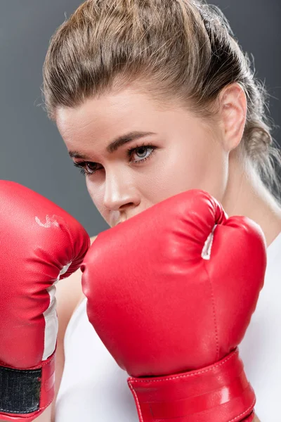 Крупный план молодой женщины в боксёрских перчатках, смотрящей в сторону изолированной на сером — стоковое фото