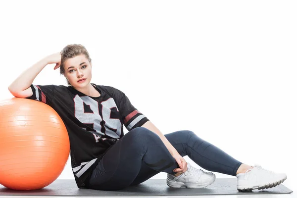 Attractive overweight woman sitting in yoga mat and leaning at fit ball isolated on white — Stock Photo