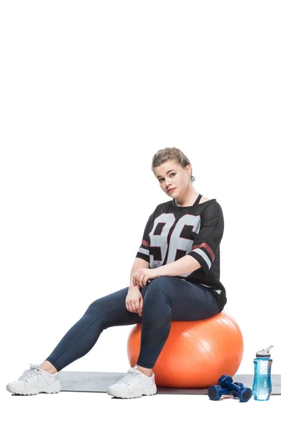 Giovane donna in sovrappeso seduta sulla palla in forma e guardando la fotocamera isolata sul bianco — Foto stock