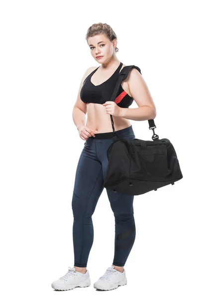 Vista de longitud completa de atractivo tamaño joven más mujer con bolsa de deporte mirando a la cámara aislada en blanco - foto de stock