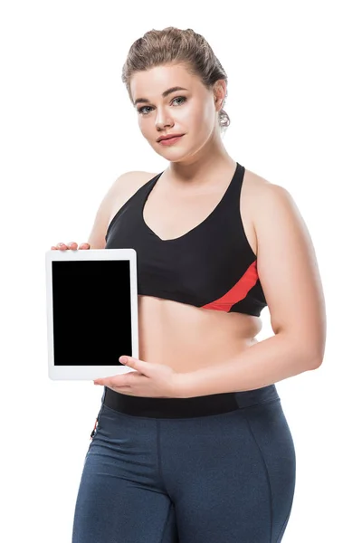 Joven mujer con sobrepeso en ropa deportiva sosteniendo tableta digital y mirando a la cámara aislada en blanco - foto de stock
