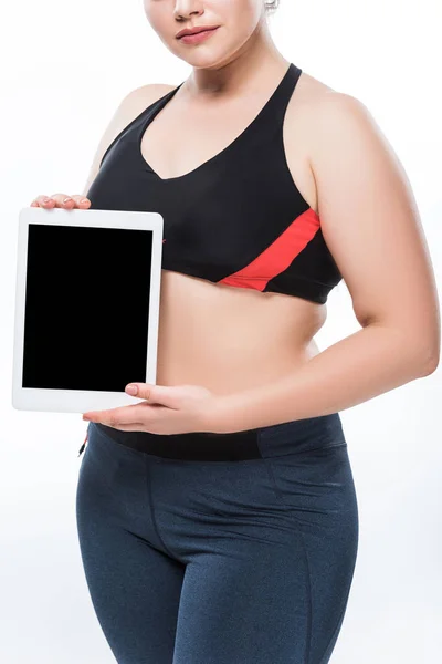 Schnappschuss einer jungen übergewichtigen Frau in Sportbekleidung, die ein digitales Tablet mit leerem Bildschirm hält, isoliert auf weiß — Stockfoto