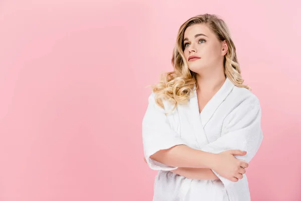 Bela jovem mulher oversize em roupão de banho de pé com os braços cruzados e olhando para longe isolado em rosa — Fotografia de Stock