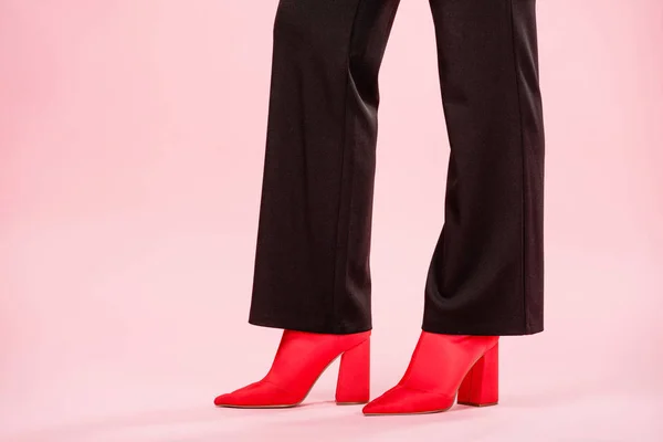 Sezione bassa della giovane donna in pantaloni neri alla moda e scarpe rosse in piedi su rosa — Foto stock