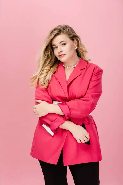 Приваблива молода жінка плюс розмір жінка в стильній рожевій куртці дивиться на камеру ізольовано на рожевому — стокове фото