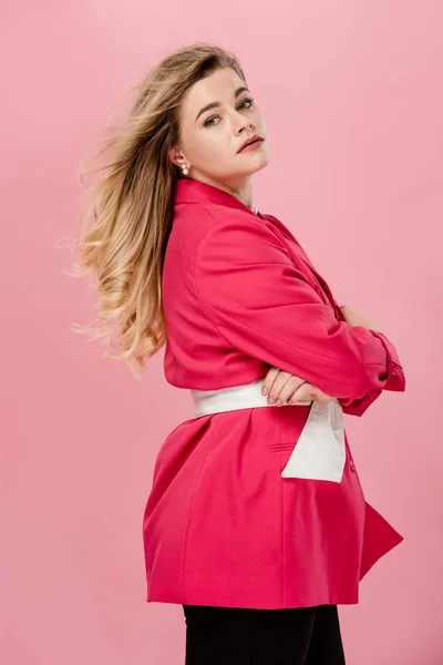 Seitenansicht der schönen stylischen übergroßen Frau, die mit verschränkten Armen steht und isoliert auf rosa Kamera schaut — Stockfoto