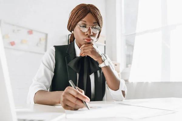 Afro-américaine femme architecte adulte dans des lunettes à l'aide d'un stylo et de travailler sur des documents au bureau — Photo de stock