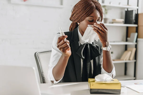Ill african american adult businesswoman suffering from cold and using tissues at desk in office — Stock Photo