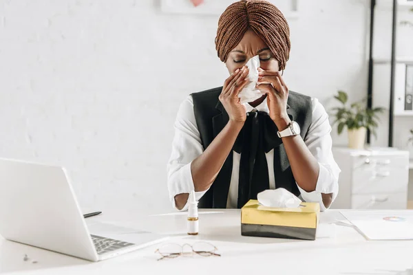 Mujer de negocios adulta afroamericana enferma que sufre de frío y el uso de tejidos en el escritorio en la oficina - foto de stock